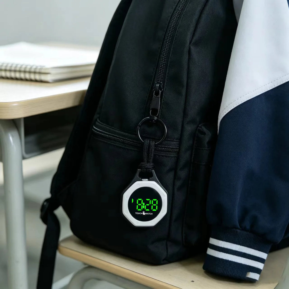 Black KAVIUR Loop Digital Bag Watch with black hanging cord and white bezel on a backpack
